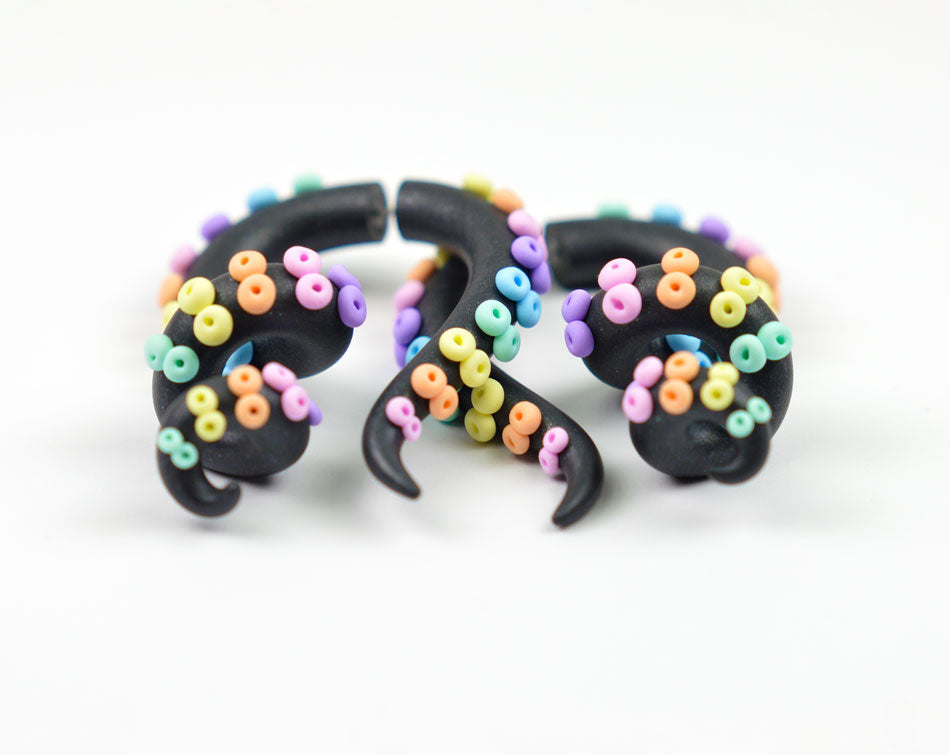 Pastel goth rainbow in the dark sky tentacle earrings and tentacle gauges by Tania Chernova. It's handmade earrings of polymer clay with pastel rainbow suction cups and black shimmer dust octopus tentacle. I make both fake gauge earrings (stud earrings or two part earrings) and ear gauges for stretched ears gauged ears.