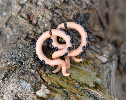 Octopus tentacle earrings in beige with metallic black dots.